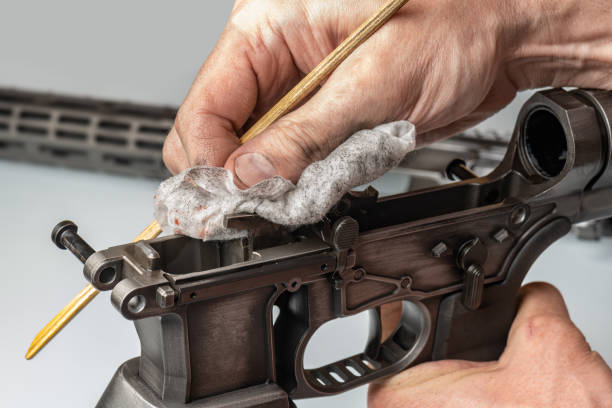 Person cleaning a rifle with a cloth and brush on a gray background